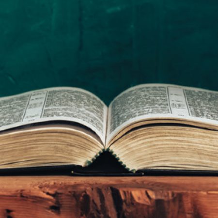 Open bible on a red old wooden table. Beautiful green wall background.