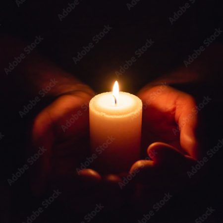 Hands holding burning candle in dark like a heart.Selective focus,black background.
